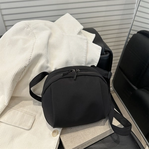 Minimalist black half-moon crossbody bag with double zippers on white corduroy jacket