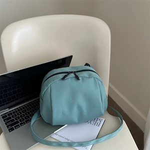 Minimalist mint green nylon shoulder bag with zipper closure on a white chair