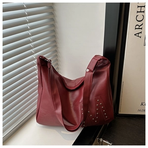 Detail of dark red faux leather tote bag showing silver rivet M logo and zip closure