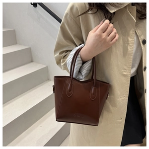 Detail of a brown leather bucket bag featuring dual handles and embossed fashion text