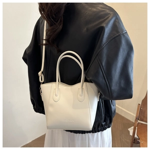 Detail of white leather bucket bag featuring FASHION embossing and adjustable strap
