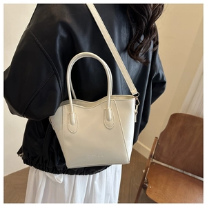 Close-up of white fashion bucket bag worn as a crossbody by a model in a minimalist setting