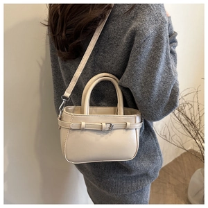 Détail d'un sac à main en cuir crème porté avec une tenue en tricot et une bandoulière