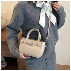 Detail of a minimalist beige crossbody square bag with decorative buckle and slim strap