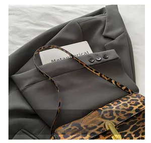 Detail der Umhängetasche mit Leopardenmuster und Goldschnalle auf grauem Anzugstoff