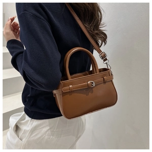 Sac bandoulière en cuir caramel avec boucle argentée porté par un mannequin en style épuré