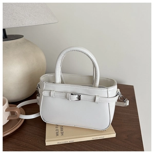 Détail d'un sac à main blanc en cuir avec boucle en métal sur une table en bois
