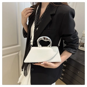 White asymmetric handbag with thick silver metal handle worn by model on shoulder