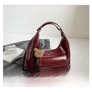 Detailed macro view of burgundy tote bag with white stitching and plush bear charm