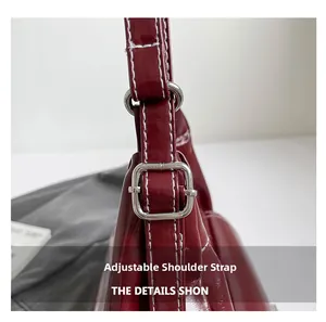 Detail of adjustable shoulder strap on wine red patent leather tote with silver buckle