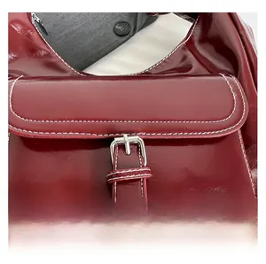 Detail of burgundy glossy leather tote bag with white contrast stitching and silver buckle