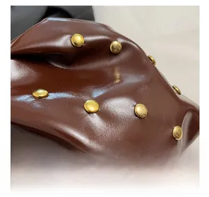 Macro shot of dark brown glossy leather with golden metal rivet details on the shoulder bag