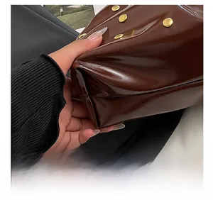 Detail of premium brown patent leather handbag with gold rivets and precise stitching