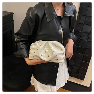 Close-up of a white cloud clutch bag with gold rivets worn by a model in style