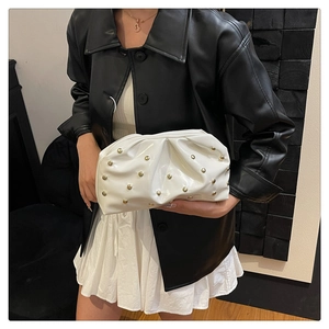 Macro shot of white pleated cloud clutch bag with gold rivets on glossy patent leather