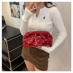 Close-up of red patent leather clutch bag with golden rivets and pleated texture details