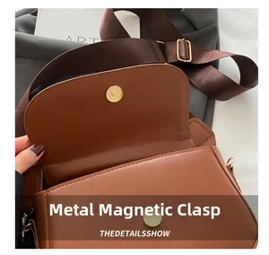 Detail of a brown leather saddle bag with gold magnetic buckle and adjustable strap