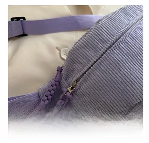 Macro detail of purple corduroy crossbody bag featuring smooth metal zipper and textured fabric