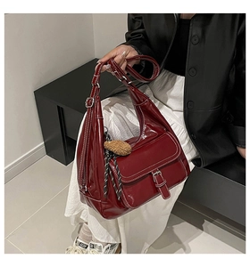 Detail of dark red tote bag featuring glossy leather, white stitching, and plush charm