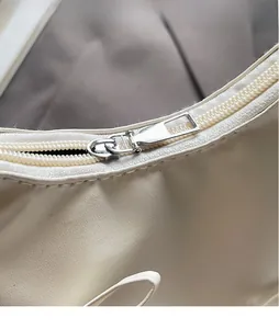 Detail of silver smooth metal zipper and leather texture on a white cloud bag