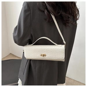 Détail du sac tressé blanc avec fermoir anneau doré élégant sur un costume gris