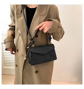 Detail of black leather crossbody bag with knot handle and gold hardware on trench coat