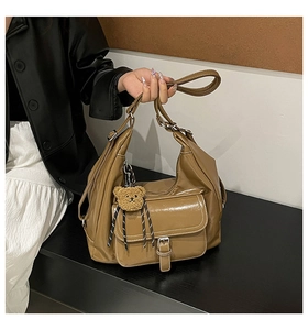 Close-up of brown leather hobo tote bag featuring a cute plush bear charm and front pocket