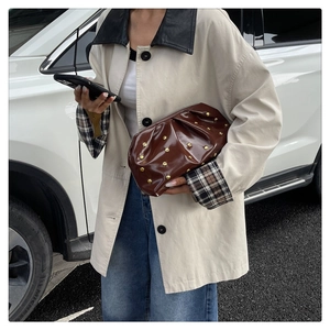 Brown pleated cloud bag with gold studs held by a model in a casual outdoor setting