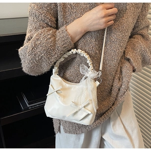 Detail of cream bow shoulder bag with lace decoration and pleated handle texture