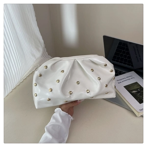 Detail of white glossy pleated cloud bag with metallic gold studs on a fashion magazine
