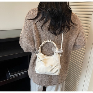 Detailed view of white pleated cloud bag featuring delicate lace ribbons and bow decor