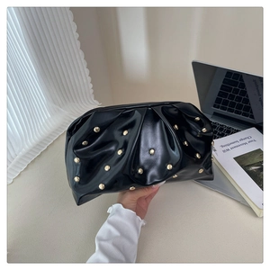 Detailed view of black pleated clutch bag with golden rivets held by a hand