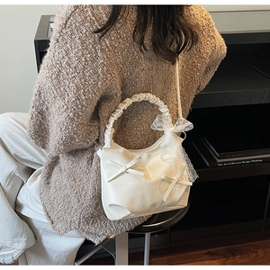 Detail of cream white pleated cloud bag featuring bow accents and lace ribbons