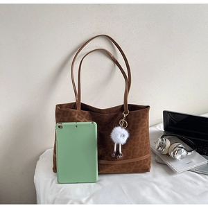 Detail view of large leopard print tote bag with plush charm in a lifestyle setup
