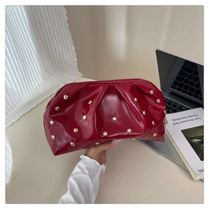 Detail of red ruched clutch bag with gold studs and glossy patent leather finish