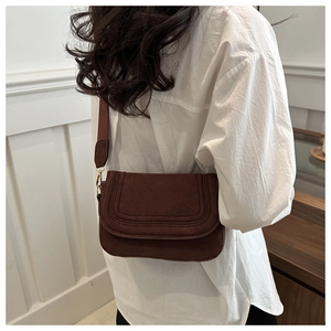 Detail of dark brown faux suede saddle bag with curved stitching and fabric strap