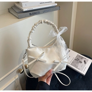 Detail of white leather dumpling bag with lace bows and ruched handle for women
