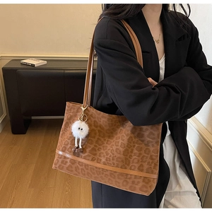 Detail of leopard print tote bag featuring brown leather straps and a plush doll pendant