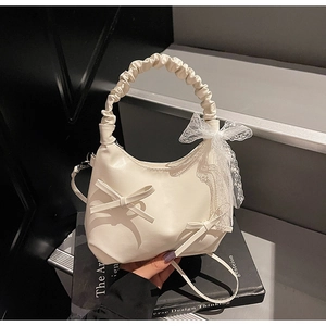 Close-up of cream-white crescent shoulder bag with pleated handle and lace bow detail