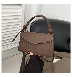 Close-up of deep brown leather handbag featuring an envelope flap and golden hardware