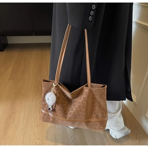 Close-up of leopard print tote bag with plush monster charm and sleek brown straps