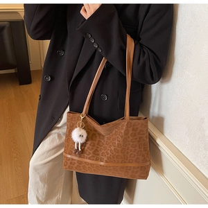 Detail of leopard print tote bag with brown leather straps and white pom-pom pendant