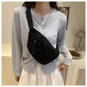 Detail of black corduroy chest bag featuring textured layers and adjustable strap buckled on model
