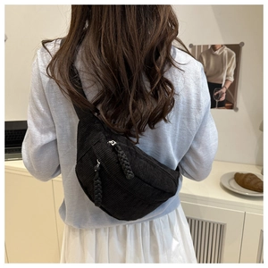 Detail of black corduroy belt bag with woven zipper pulls worn by model in home setting