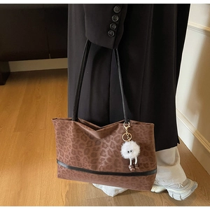 Close-up of leopard print tote bag with black straps and white plush monster charm