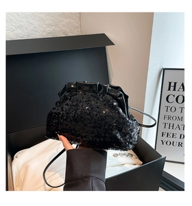 Close-up of black sequined dumpling tote bag with sleek leather trim in a premium gift box