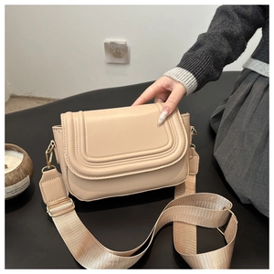 Detail of beige saddle bag with U-shaped embossed flap and wide woven shoulder strap