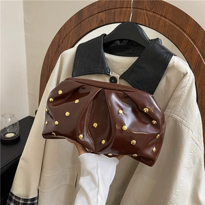 Dark brown pleated clutch bag with gold studs and glossy finish in a lifestyle setting