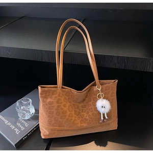 Detail of leopard print tote bag with plush charm and long shoulder straps on a display