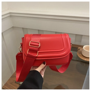Detailed view of a red leather saddle bag with wide fabric strap and gold buckles
